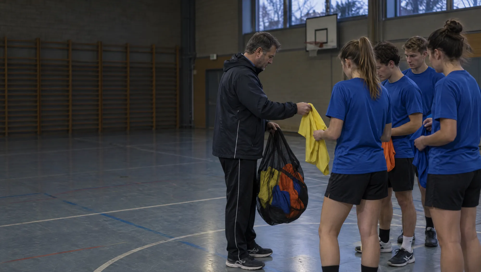 Trainer verteilt in der Sporthalle bunte Leibchen an sein Team
